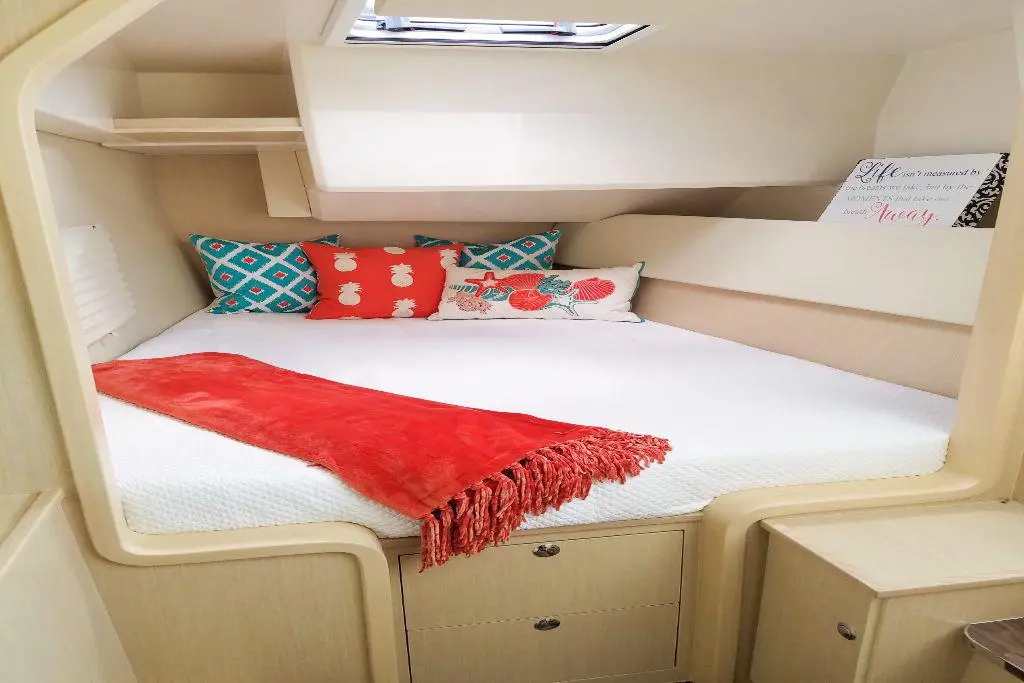 Cozy boat cabin featuring a double bed with colourful cushions, a red throw, and a decorative sign, ideal for relaxation.